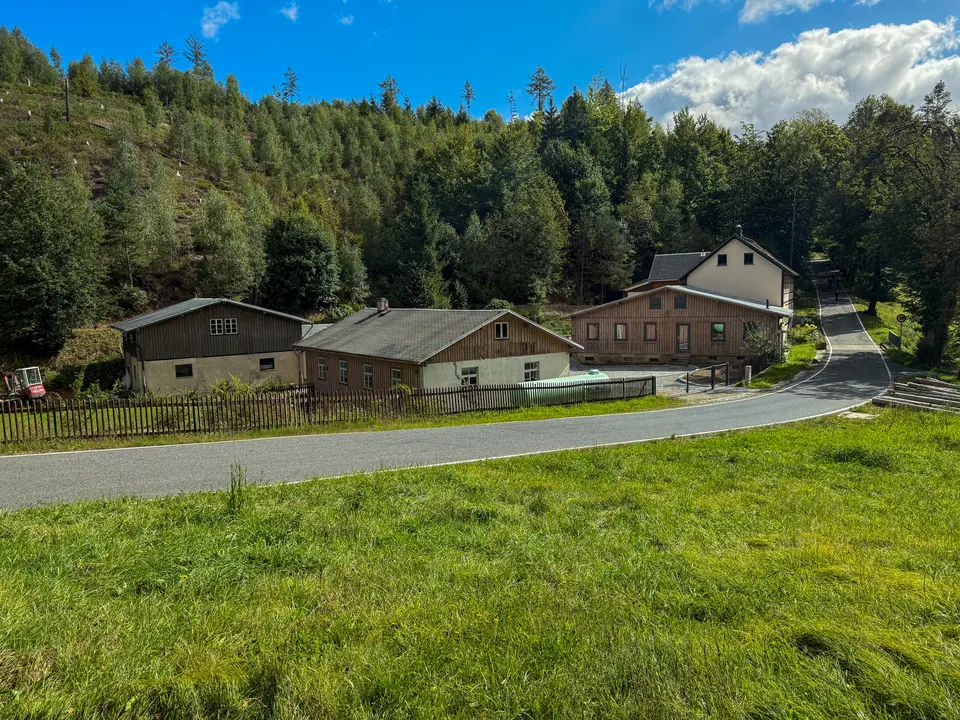 Die Gebäude der Gnauckmühle an der Dorfstraße vor bewaldetem Hang