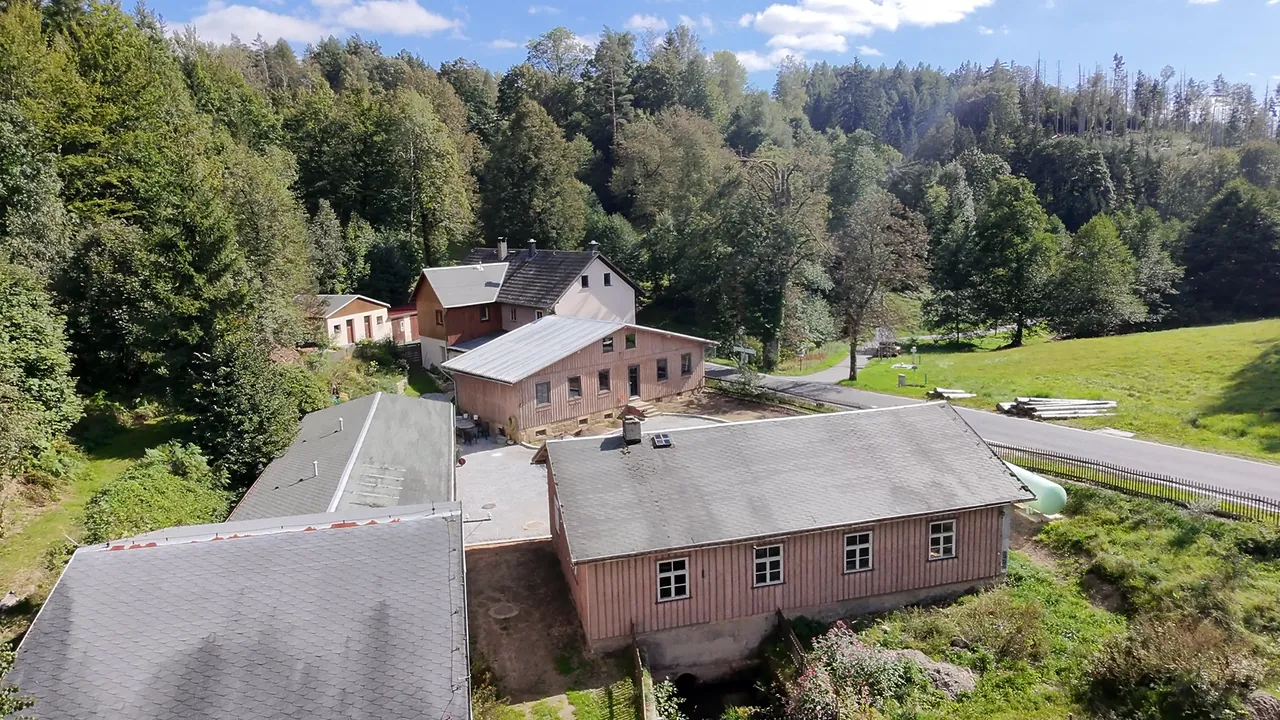 Luftaufnahme des Hofensembles der Gnauckmühle: Hauptgebäude, Holzhäuser, Langgebäude und Scheune zwischen Wald und Wiesen