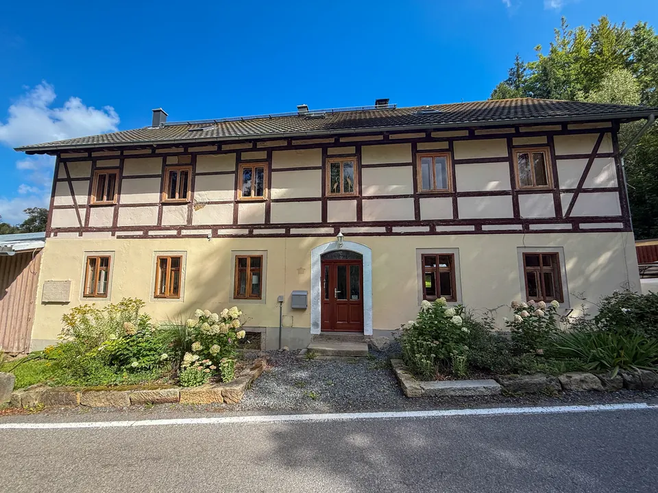 Das Fachwerk-Hauptgebäude der Gnauckmühle mit roter Haustür und blühenden Hortensien